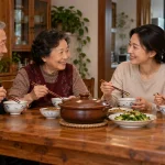 Three generations sharing a meal with a covered earthenware pot and bowls in a home dining room
